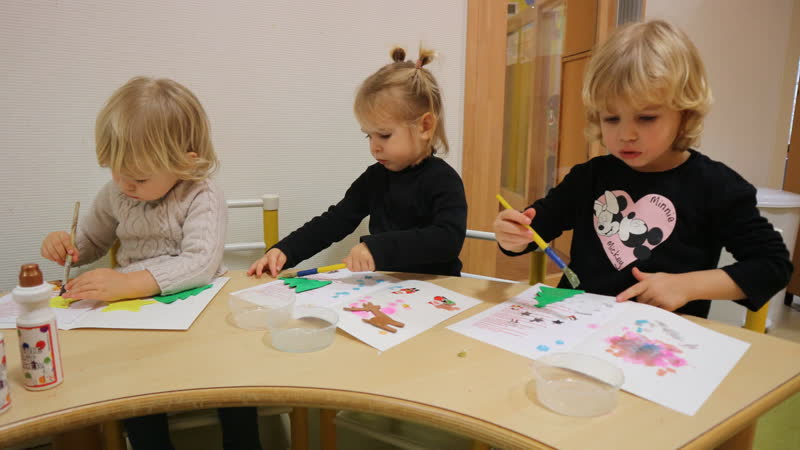 Trois enfants peignent et collent à une table