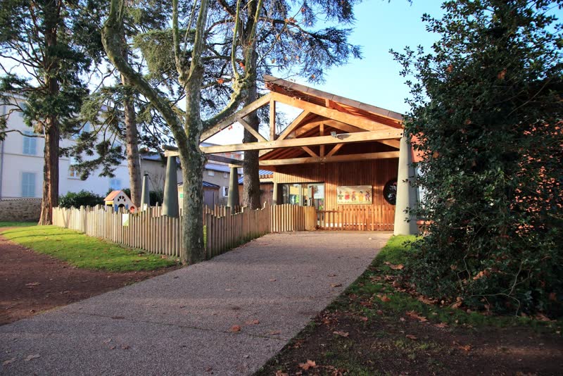 L'entrée de la crèche : un bâtiment à charpente en bois, une allée et des grands arbres