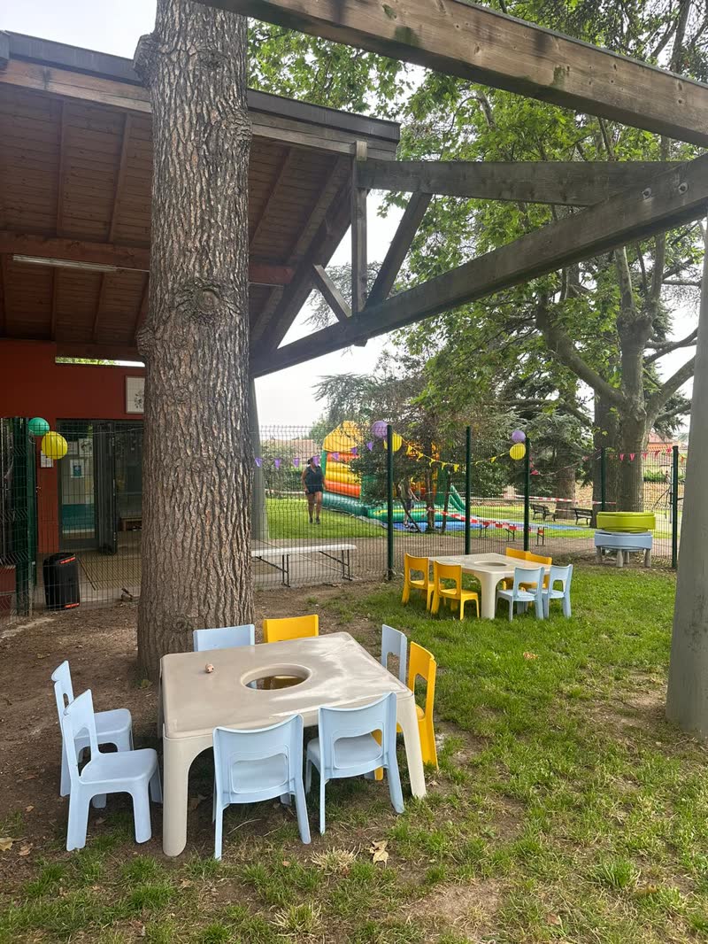 Le jardin de la crèche : petites tables et chaises d'enfant sous un grand arbre