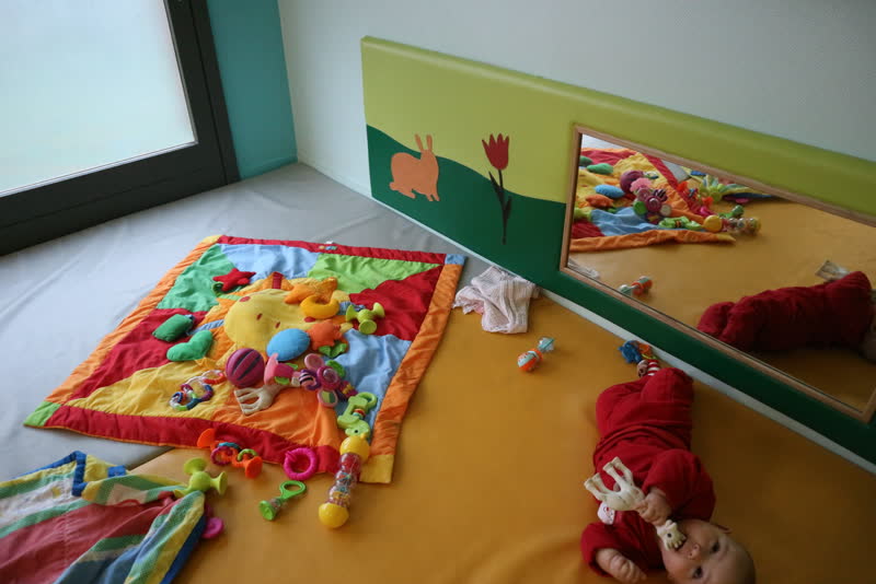 Des bébés jouent sur un grand tapis d'éveil coloré, près d'un miroir bas